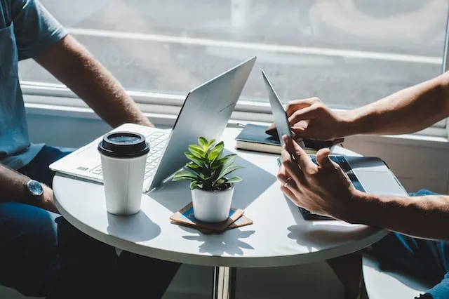 A photo of laptop on a small round cafe table with 
                                        two people sat around it